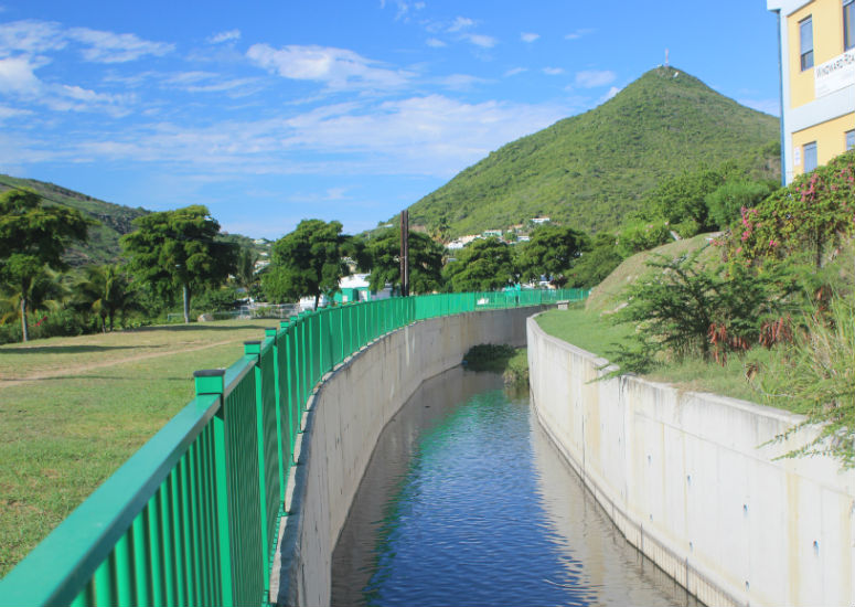 Rolandus Channel with a green fence next to it and a big green hill in the background