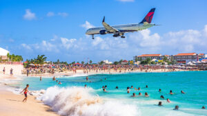 Plane spotters watching a plane fly over Maho Beach while swimming in the Caribbean Sea