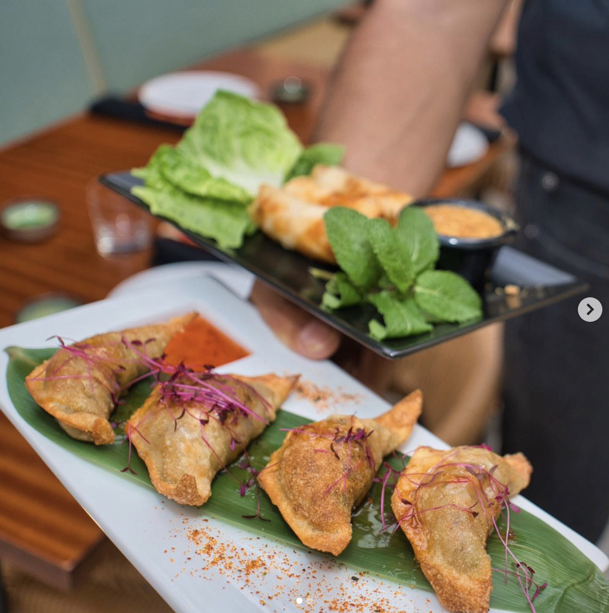 A person holding two plates of food in front of a brown wooden table