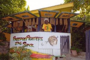 A Rastafari man with a head and a yellow shirt standing in the Ital shack 