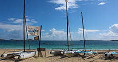 Catamarans for rent lying on Orient Bay Beach with flags waving over them in windy weather 