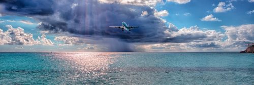 Airplane flying over sea with clouds and sun in the background