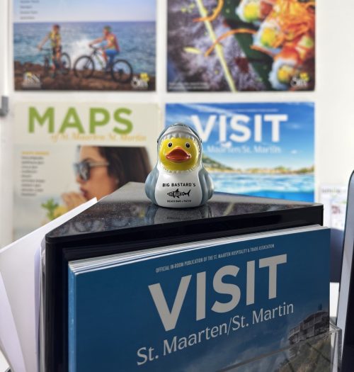 Big Bastard's Beach Bar mascotte Snarky posing in front of visitstmaarten magazines