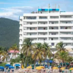 Atrium Beach Resort tower with green St Maarten hills in the background and Kim Sha beach and palm trees in front