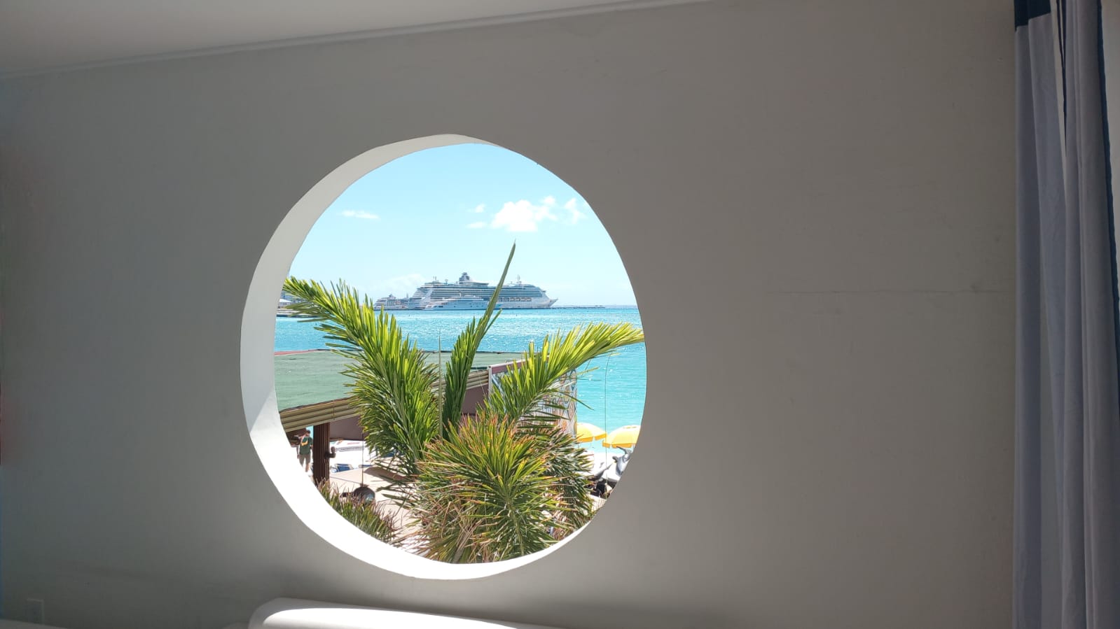 Circle window view with palmtree and cruiseship in the background