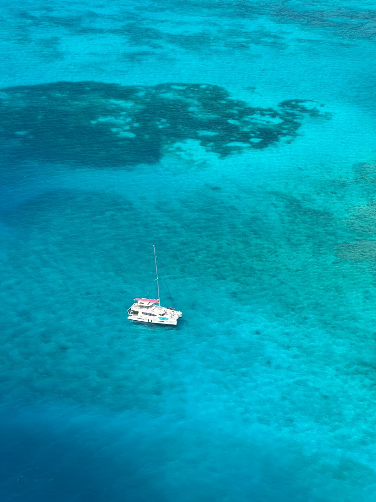 Helicopter point of view of lonely catamaran sail boat in a turqouise sea