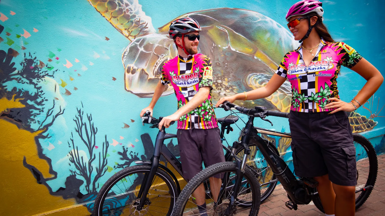 Cyclists pause in front of a colorful sea turtle mural in St. Maarten.