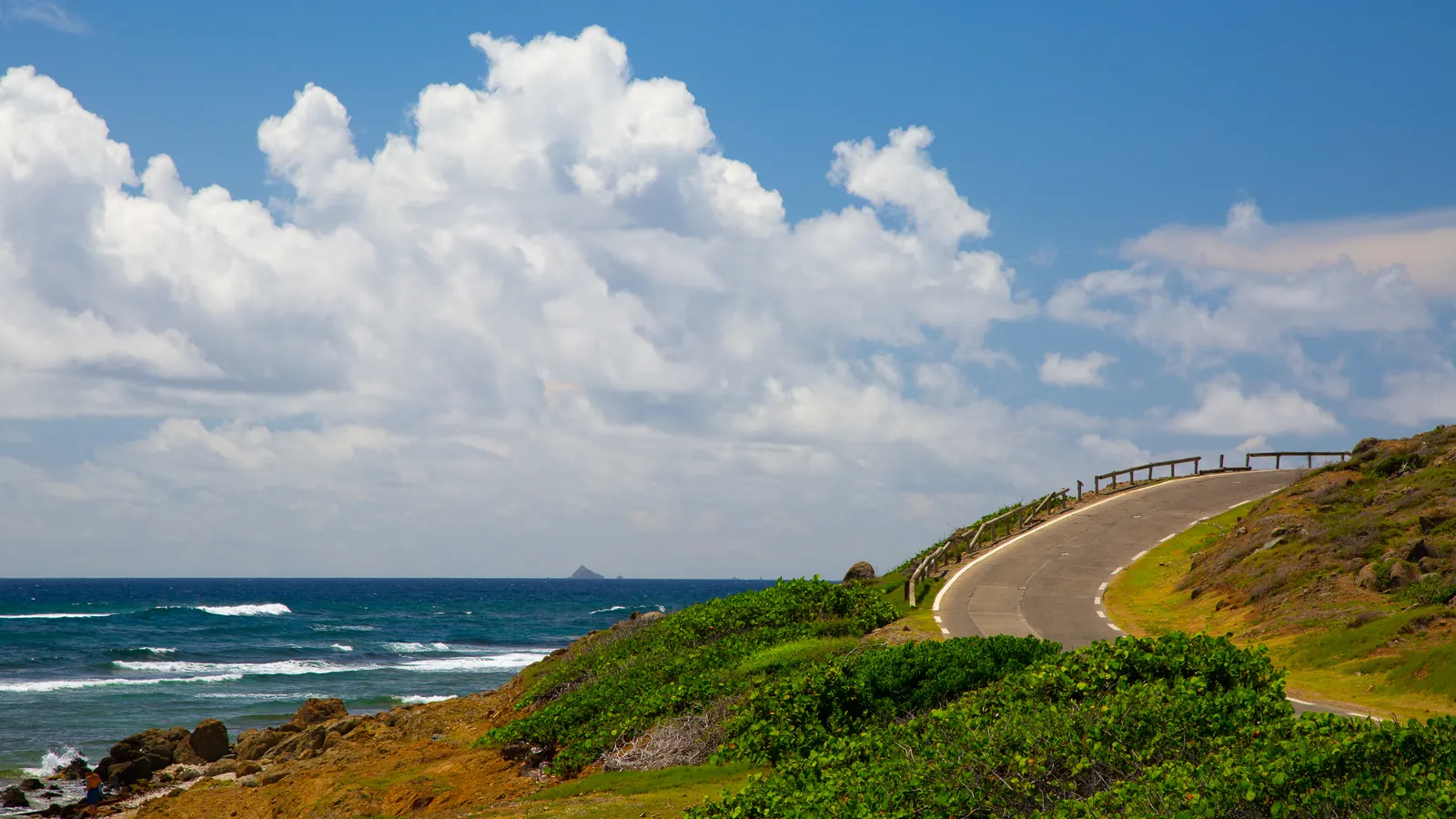 Coastal road curves past green hills and Atlantic waves at Babit Point, St. Maarten.