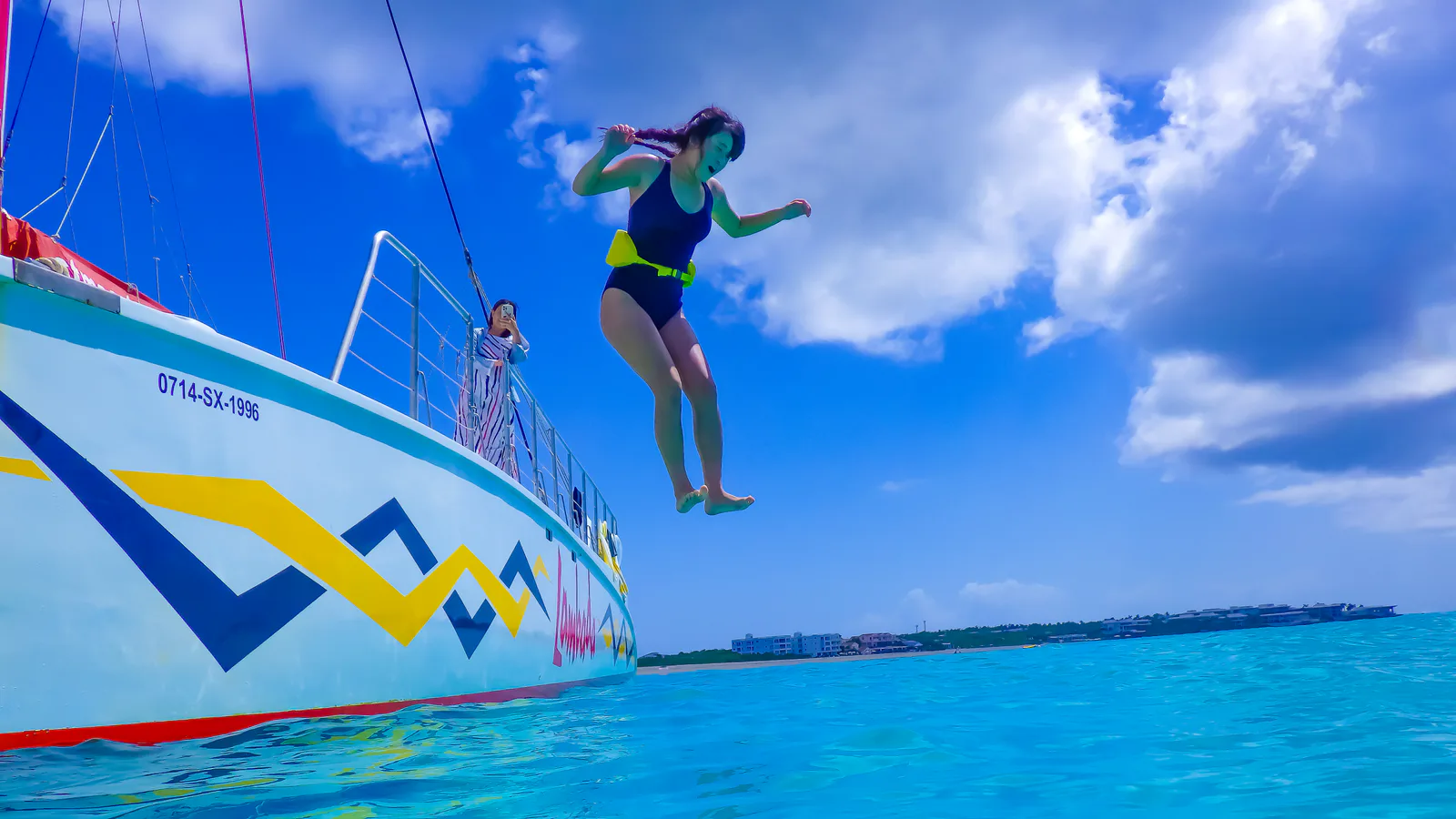 Traveler wearing a flotation belt jumps from a catamaran into turquoise water off St. Maarten.