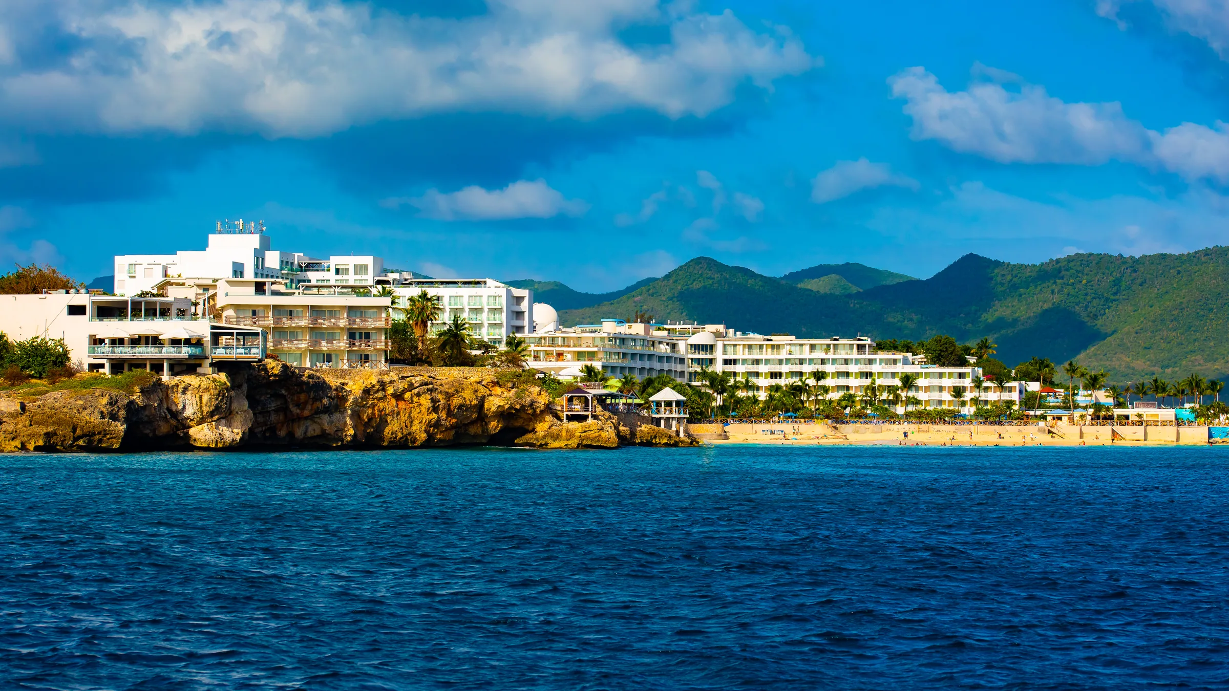 Seafront resort buildings along Maho Bay with St. Maarten hills behind them.