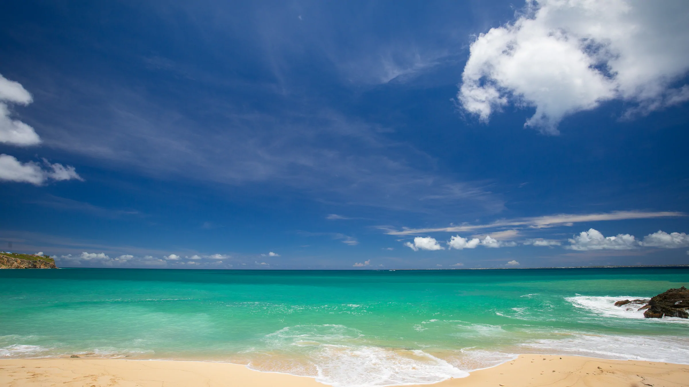 Turquoise sea and pale sandy shoreline beneath a blue sky.