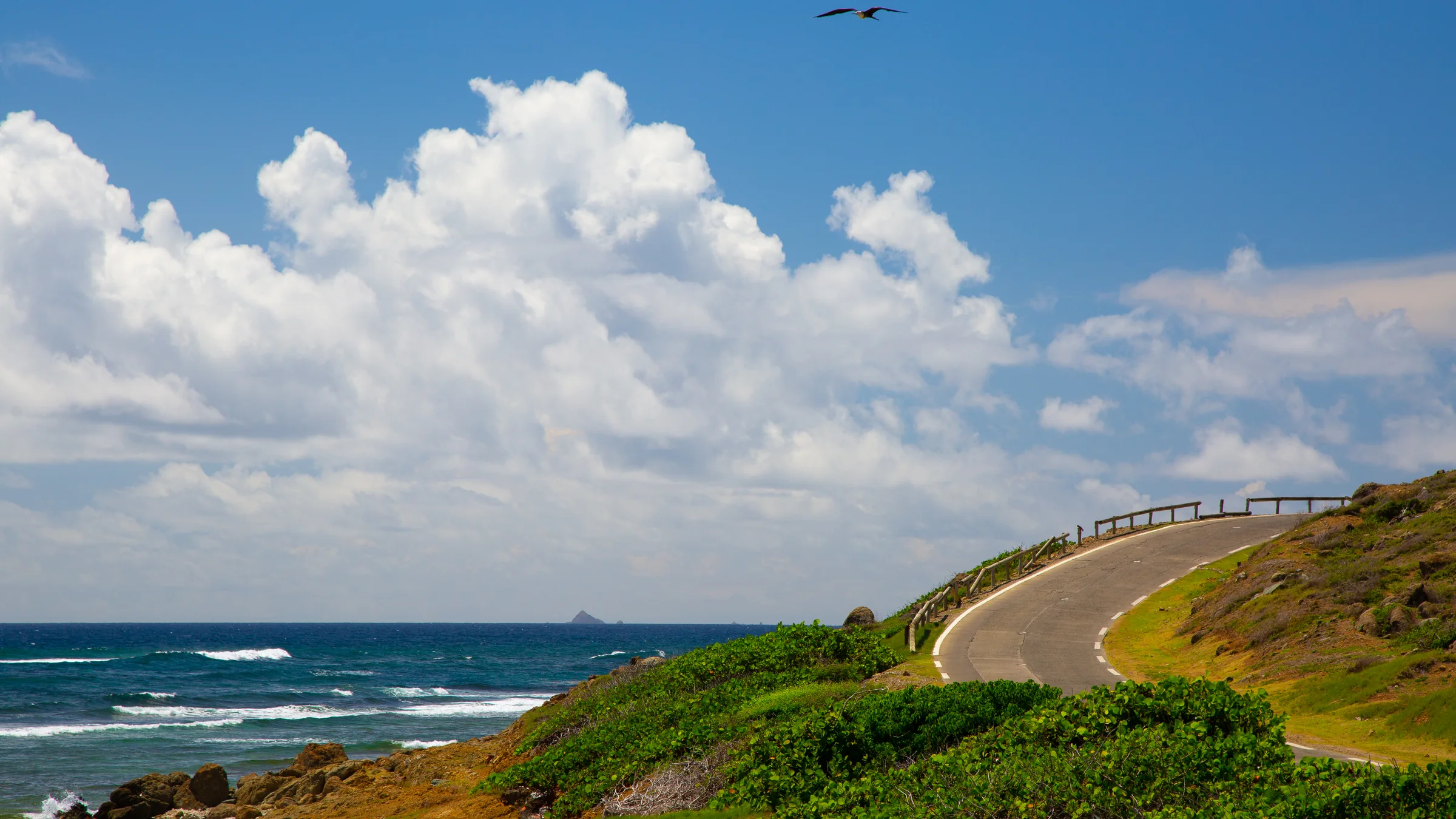 Coastal road curves past green hills and Atlantic waves at Babit Point, St. Maarten.